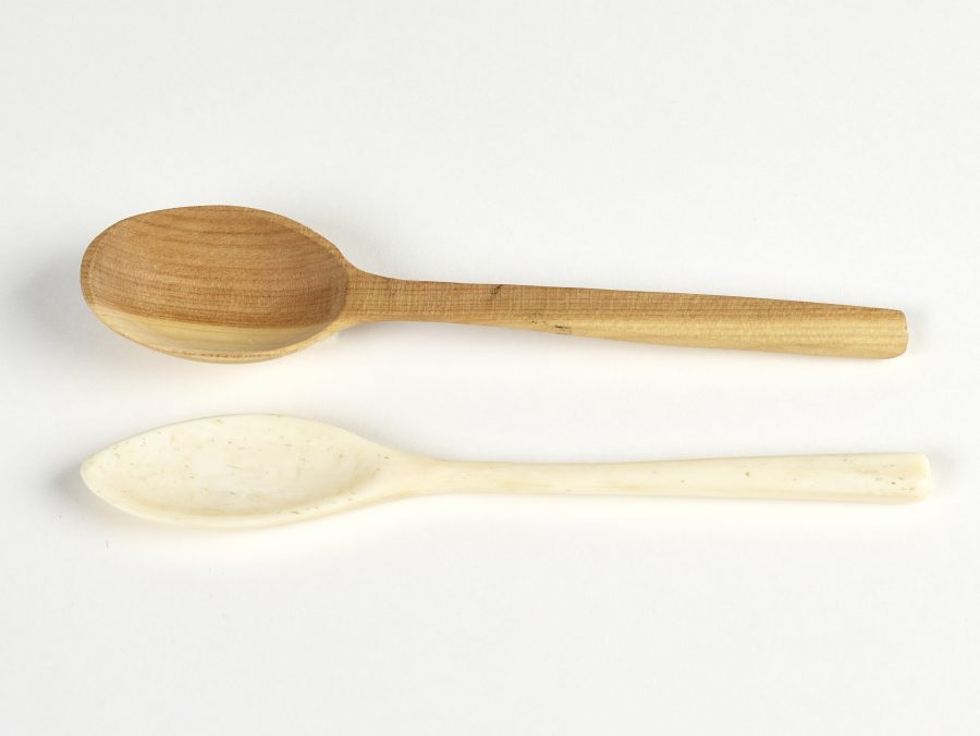 A carved wooden spoon and a carved bone spoon