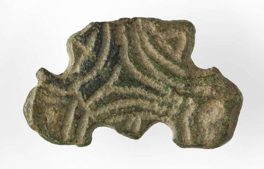 Trefoil Mount. A broken fragment from a trefoil mount. The central section is triangular and has two intact expanding arms. Decoration is simple line pattern mirroring the general shape. Some evidence of rivets on the arms. Find Spot: Torksey, Lincolnshire. Copper alloy, 700-899. Anglo-Saxon. (c) The Fitzwilliam Museum